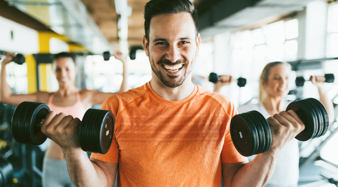 Goofy-Male-Lifting-Light-Weight-Dumbbell-Two-Females-In-The-Back-Dumbbell-Overhead-Press