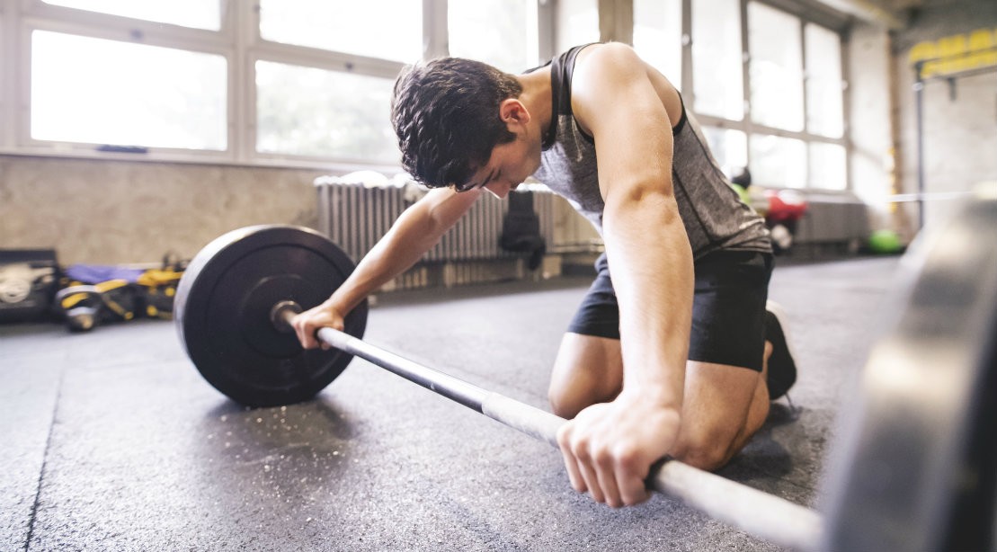 Man exercising with barbell taking break Tired man working out at gym